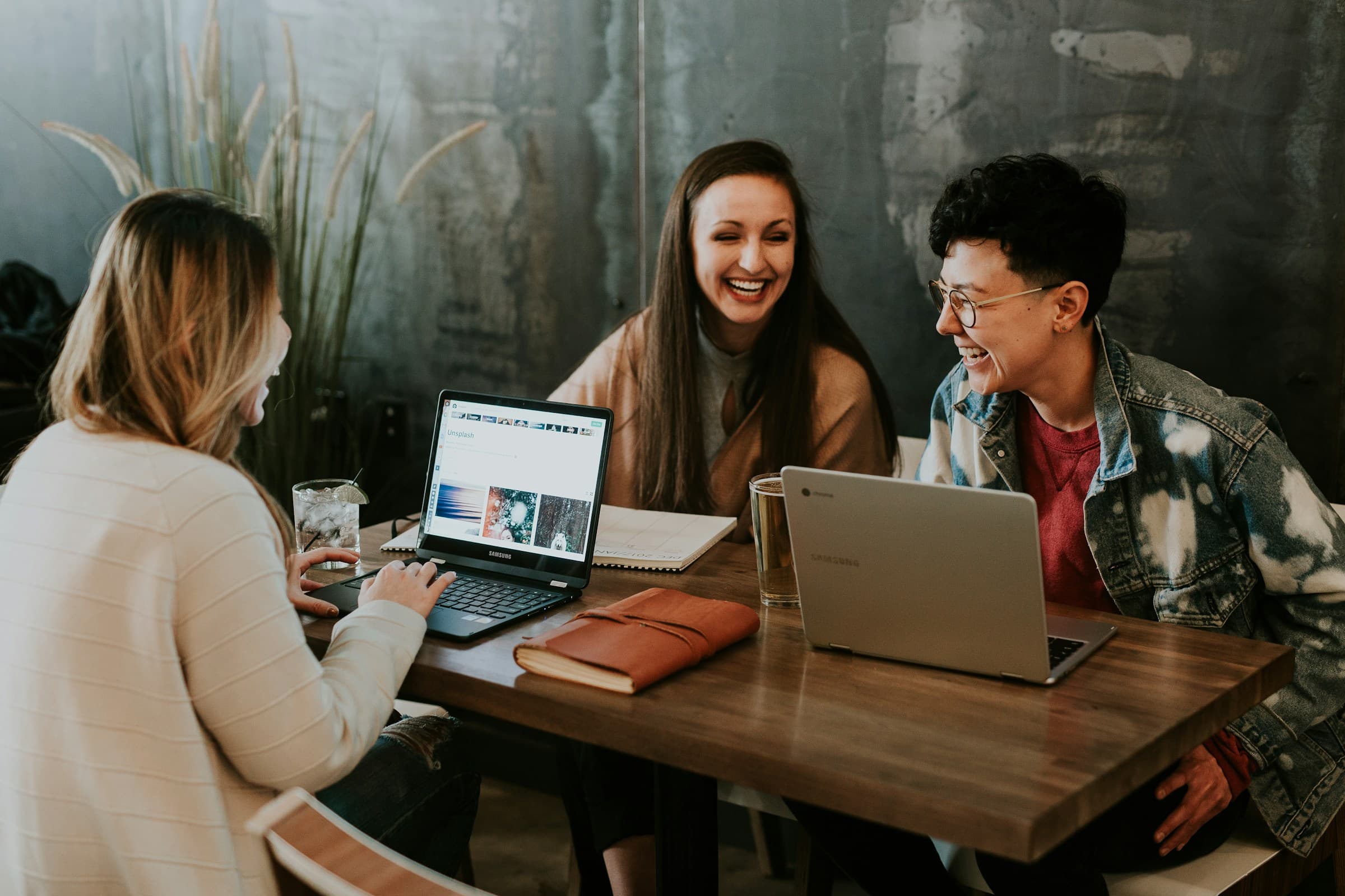 Three colleagues laughing together at a table with laptops